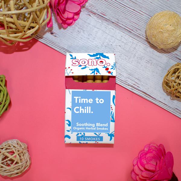 Image Description: A cardboard smoke pack titled Time to Chill, referring to the herbal smoking blend that the 10 smokes inside are filled with. Beneath the title are the words Soothing Blends, & Organic Herbal Smokes. The box is decorated with blue floral shapes designed to look like the ingredients inside: Marigold, Klip Dagga, Rosemary, Mullein, Skullcap & Lavender. Peeking out from the pack are 10 herbal cigarettes, also known as Herbal Spliffs, Herbal Smokes, Herbs & Flowers Prerolls, or Herb Tokes.